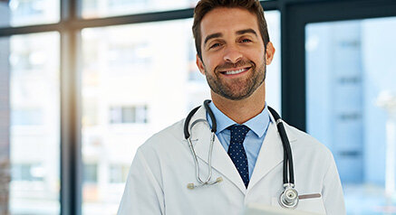 Junger Arzt mit Stethoskop und weißem Arztkittel lächelt.
