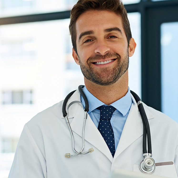 Junger Arzt mit Stethoskop und weißem Arztkittel lächelt.